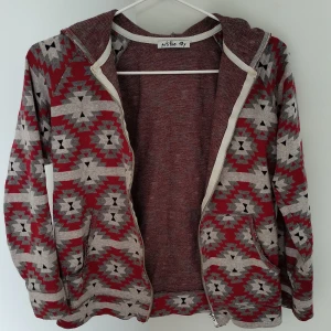 Mönstrad hoodie från Petitbo, röd/grå - Snygg hoodie från Petitbo i rött och grått med coolt geometriskt mönster. Tröjan har huva, dragkedja framtill och två fickor. 