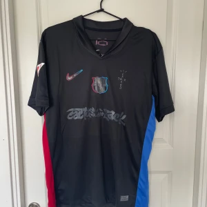 FC Barcelona x Cactus Jack Nike tröja L - Säljer en svart FC Barcelona x Cactus Jack fotbollströja från Nike i storlek L. Tröjan har korta ärmar, klubbmärke och Nike-logga framtill, samt grafiska detaljer och texten 'Cactus Jack'. Sidorna har röda och blå paneler. Tillverkad i lätt och ventilerande polyester. Helt ny aldrig använd storlek L