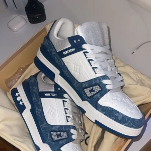 Louis Vuitton blåvita sneakers - Snygga Louis Vuitton sneakers i vitt och blått med klassiskt LV-monogram på både tunga och sidor. Skorna har vita snören, rund tå och detaljer i präglat skinn samt denimliknande material. Perfekt för dig som vill sticka ut med exklusiva och trendiga sneakers. Har ej lådan eller kvittot kvar