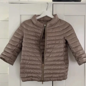 Beige dunjacka från Herno - Snygg beige dunjacka från Herno med trekvartsärm och hög krage. Jackan har quiltad design, dragkedja framtill och en lätt oversized passform. Perfekt för dig som vill ha en stilren och lätt jacka med modern känsla.