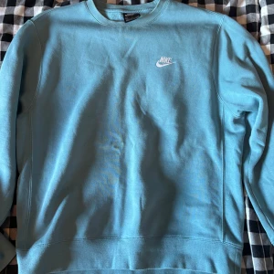 Blå crewneck från Nike i bomull - Snygg ljusblå crewneck från Nike med klassisk logga broderad på bröstet. Tröjan har rund halsringning och långa ärmar, tillverkad i mjuk bomullsmix som är skön att ha på sig. Perfekt för en chill och sportig stil.