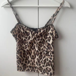 Leopardmönstrad linnetopp med spets - Säljer en leopardmönstrad linnetopp med tunna axelband och söt svart spetskant upptill. Toppen har en liten rosett framtill och är i glansigt material som ger en lyxig känsla. Perfekt för dig som vill sticka ut med ett djurmönster och trendiga detaljer.❗️Nypris 200❗️