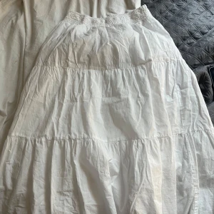 Vit långkjol från Mango med resår - Superfin vit långkjol från Mango med smockad resår i midjan och volangiga lager. Kjolen är i tunn, luftig bomull och har en mjuk underkjol. Perfekt för varma dagar när du vill ha en kjol som är luftig. Den är kort för mig och därför säljer jag den.