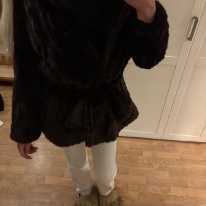 Mörkbrun äkta pälsjacka från A.C. Bang - Säljer en lyxig mörkbrun pälsjacka från A.C. Bang med bälte i midjan. Jackan har en klassisk omlottmodell och är helfodrad med mjukt tyg. Perfekt för dig som vill ha en elegant och tidlös look under kyliga dagar.