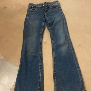 Blå bootcut jeans från Gina Tricot - Snygga blå jeans från Gina Tricot i bootcut-modell med klassiska fickor och markerade sömmar. Jeansen har låg midja och är tillverkade i jeansmaterial med en cool tvättad look. Perfekta för dig som gillar retrovibbar och vill ha ett par jeans med lite extra attityd.