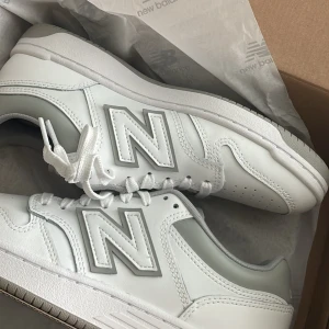 New Balance BB480  - Snygga New Balance BB480 sneakers i vitt och ljusgrått med klassisk siluett och stora N-loggor på sidorna. Skorna har snörning, platt sula och är tillverkade i skinn och syntet. Skorna är helt oanvända! 