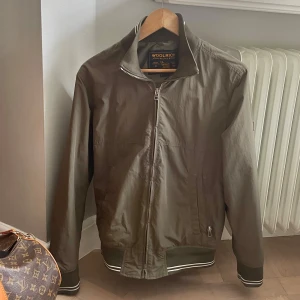 Woolrich jacka - Woolrich” trendig vardagsjacka modell, snygg grön färg som blänker lite lätt i solen. En jacka man kan ha över tshirten eller bygga lager på lager.  Modellen på bilden är 185 cm. Inköpt för 2899:- ifjol utomlands. Unik modell, som inte säljs inte längre. En favorit.  ‼️ Inga! defekter, som ny ‼️ 