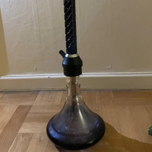 Komplett vattenpipa med tillbehör - Säljer en vattenpipa i glas och metall med svart bas och spiralformad hals. Medföljer slang, kolbricka, elplatta, tänger, tobak från Darkside, Musthave och NextGen samt kol och lera huvud. Perfekt för dig som gillar att röka vattenpipa med olika smaker.