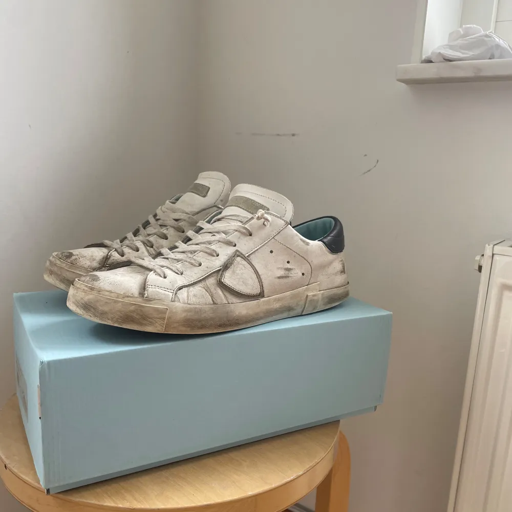Säljer ett par vita sneakers från Philippe Model med grå detaljer och svart häl. Skorna har snörning, rund tå och platt sula. Klassisk design med diskret logga på sidan och bekväm innersula. Skorna är väl använda och har många slittningar men fungerar fortfarande fint,  okej skick storlek 42. Kengät.