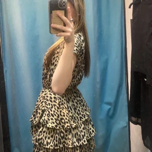 Leopardmönstrad volangklänning - Säljer en kort klänning med leopardmönster och volangdetaljer. Klänningen har korta ärmar, rund halsringning och markerad midja med lätt rynk. Man knäpper den i nacken. 💞
