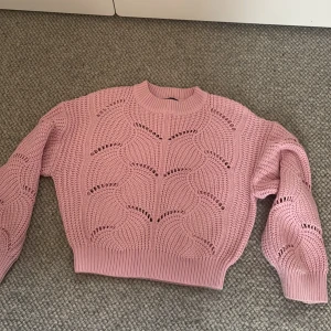 Rosa stickad tröja från Gina Tricot - Säljer en ljusrosa stickad tröja från Gina Tricot i storlek XS. Tröjan har ett snyggt hålmönster, ribbade muddar och är croppad i modellen. Perfekt för lager-på-lager och ger en söt touch till din outfit.