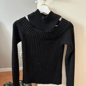 Svart ribbad stickad tröja från NA-KD - Säljer en svart ribbstickad tröja från NA-KD i storlek XS. Tröjan har lång ärm och en hög, bred polokrage som ger en snygg och modern look. Perfekt för kyligare dagar och enkel att matcha med olika outfits.