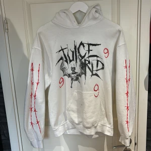 Vit Juice WRLD hoodie med tryck - Vit hoodie med Juice WRLD-tryck och fladdermusmotiv på bröstet samt röda taggtrådsdetaljer längs båda ärmarna. Stor luva och magficka framtill. Snygg streetwear-stil för dig som gillar unika prints. ( SÄLJS EJ LÄNGRE ) (Obs saknar snören) Säljs för 250