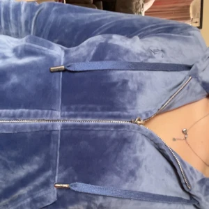 Blå velour kofta från Juicy Couture - Supermjuk och mysig blå kofta i velour från Juicy Couture. Klassisk modell med fickor framtill, dragkedja och justerbara snören i huvan. Perfekt att slänga på sig till vardags eller som en del av ett set! Obs: dragkedjan är lite trasig, men koftan funkar ändå fint.💗