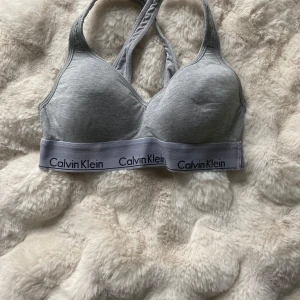Grå bh från Calvin Klein - Säljer en grå bh från Calvin Klein med bred resår och logga runt om. Tillverkad i bomullsmix för extra komfort. Köpt för 300 kr