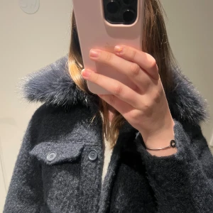 Marinblå kappa med fuskpäls - Säljer en mörkblå kappa med fluffig fuskpäls vid kragen. Kappan har knappar framtill och fickor med lock. 