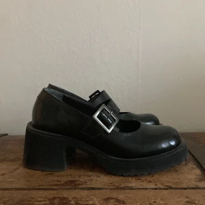 Chunky svarta Mary Jane skor med spänne - Säljer ett par chunky svarta Mary Jane skor  med bred klack och silverfärgat spänne. Skorna har rund tå och platt sula, perfekta för dig som gillar en edgy och stilren look.