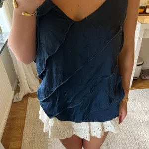 Mörkblå linnetopp med vågiga detaljer - Säljer en mörkblå linnetopp med smala axelband och vågiga sömdetaljer framtill. Toppen har en lätt v-ringning och är tillverkad i ett tunt, mjukt material som känns svalt mot huden. Perfekt för varma dagar. Fått sy ihop bandet (se sista bild) nypris 500, mitt 300. Pris kan gå att diskutera vid snabb affär☺️🩷