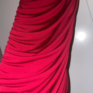 Mörk röd  - Säljer en snygg mörk röd kjol med rynkade detaljer längs sidorna. Kjolen har en tight passform och är tillverkad i ett mjukt, stretchigt material som sitter skönt på kroppen. 