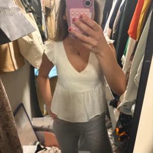 Vit blus med spetsdetaljer - Säljer en söt vit blus med v-ringning och spets på axlarna. Blusen har en lätt volang nertill och är ärmlös, perfekt för varmare dagar. Passar till både jeans och kjol. sSkriv för fler bilder och info🥰