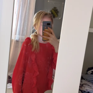 Röd blus med volangdetaljer - Säljer en röd blus med långa ärmar och volangdetaljer framtill. Blusen har rund halsringning och stängs med dragkedja i nacken. Perfekt för dig som vill ha en färgstark och trendig topp till garderoben.❤️❤️