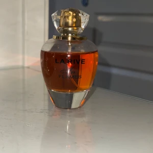 La Rive In Flames Eau de Parfum - En elegant parfymflaska från La Rive med namnet In Flames. Flaskan är rund med en klar glasbotten och guldigt lock. Parfymen har en varm, bärnstensfärgad vätska och rymmer 90 ml Eau de Parfum.