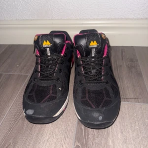 Svarta och rosa sneakers från Monitor - Säljer ett par svarta sneakers från Monitor med rosa och vita detaljer. Skorna har snörning, meshpartier och en slitstark sula. Perfekta för dig som vill ha bekväma och sportiga skor med snygg färgkombination.