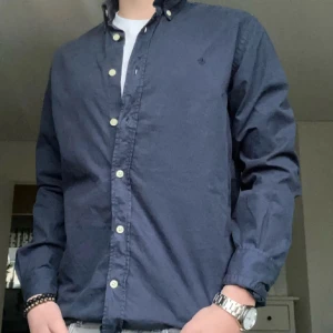 Mörkblå skjorta från Morris - Klassisk mörkblå skjorta från Morris med button-down krage och broderad logga på bröstet. Skjortan har vita knappar och lång ärm, perfekt nu inför sommaren. Tillverkad i bomull för en skön känsla.