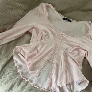 Ljusrosa blus  - Supersöt ljusrosa blus från Gina Tricot med långa ärmar, spetskant längs urringningen och framtill samt en liten rosett. Använd endast ett fåtal gånger🩷