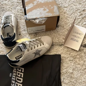 Golden Goose med glittrig stjärndetalj - Säljer ett par vita Golden Goose sneakers med grå snörning och silverglittrig stjärna på sidan. Skorna har storlek 38 och kommer med prislapp och låda. Priset går att diskutera vid snabb affär:)