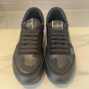Valentino Rockrunner sneakers i svart camo - Säljer ett par svarta Valentino Rockrunner sneakers med kamouflagemönster. Skorna har svarta snören, rund tå och platt sula. Märkeslogga på plösen och detaljer i både mocka och skinn. Kommer med originalkartong.