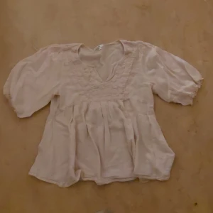 Ljusbeige blus med v-ringning från KappAhl - Säljer en ljusbeige blus från KappAhl med v-ringning och trekvartsärmar. Blusen har fina rynkade detaljer framtill och är tillverkad i ett lätt, luftigt material. Perfekt för vår och sommar!