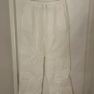 Vita linnebyxor med dragsko - Säljer ett par vita linnebyxor med resår och dragsko i midjan. Byxorna har en avslappnad passform och raka ben, perfekta för varma dagar. De har fickor i sidorna och är tillverkade i ett lätt och luftigt linnematerial. Rosa små fläckar av en penna som jag inte lyckats få bort! 