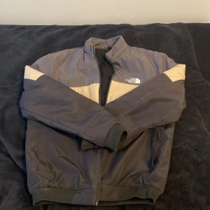 Svart och beige jacka från The North Face - Säljer en svart jacka från The North Face med beige detaljer över axlarna. Jackan har dragkedja, ribbade muddar och quiltat foder på insidan. Perfekt för kyligare dagar och har en sportig look.