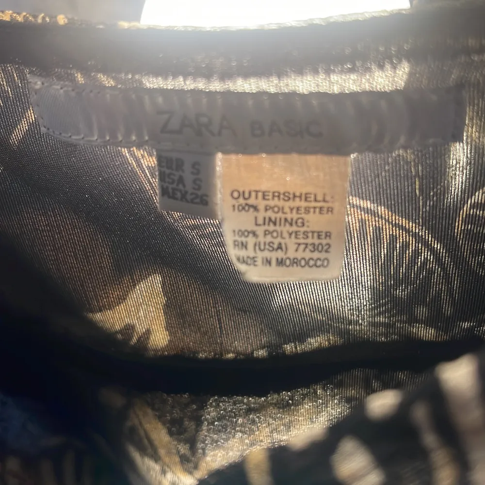Sitter som xs-xxs. Säljer en svart och beige linnetopp från Zara med tropiskt bladmönster. Toppen har smala axelband, omlottkänsla och knyt i sidan. Tillverkad i 100% polyester, perfekt för varma dagar.. Yläosat.