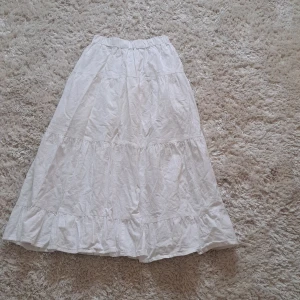 Vit långkjol  från SHEIN - Säljer en vit långkjol från SHEIN i storlek XS. Kjolen har flera volangpartier och resår i midjan för en bekväm passform. Perfekt för dig som gillar en luftig och somrig stil. Dock så fins det en liten fläck på baksidan men det är inget som synd tydligt.