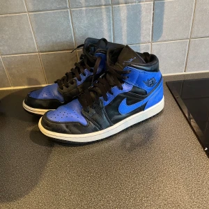 Nike Air Jordan mid  - Säljer ett par Nike Air Jordans i svart och blå med klassisk design och vit sula. Skorna har snörning och är tillverkade i skinn med tydliga Nike-loggor på sidan och tungan. Perfekta för dig som gillar streetwear och sneakers med ikonisk look. Köpte dem för 2000kr och har knappt använt dem. Pris kan diskuteras.