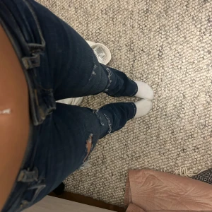 Mörkblå jeans med slitningar - Snygga mörkblå jeans med slitningar på låren och knäna. De har en klassisk femficksdesign och knappgylf. Perfekta för en avslappnad stil.