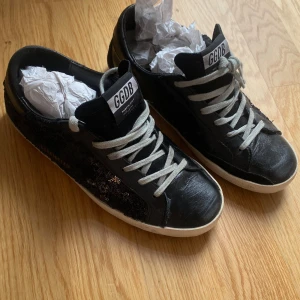 Svarta sneakers från Golden Goose strl 37 - Säljer ett par svarta Golden Goose sneakers med vita snören och vit sula. Skorna har paljettdetaljer på sidorna och GGDB-logga på plösen. 