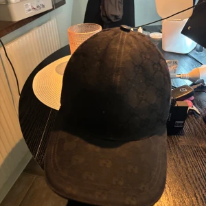 gucci keps svart - Säljer en svart keps från Gucci med diskret GG-monogram över hela kepsen och klassiska röd-gröna ränder på sidan. Justerbar rem baktill och etikett med logga på insidan. Passar dig som gillar exklusiva accessoarer. Box och kvitton medföljer 