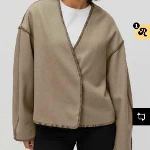 Beige omlottjacka från Stockh lm - Säljer en beige omlottjacka från Stockh lm med markerade sömmar i mörkare ton. Jackan har lång ärm, rak passform och är tillverkad i ett mjukt material som känns lite som ull. Strl Xs i princip ny