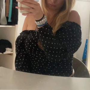 Svart offshoulder topp med vita prickar - Säljer en svart offshoulder blus med vita prickar. Toppen har långa ärmar och en croppad passform. Passar xs/s