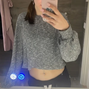 Grå croppad stickad tröja - Säljer en grå croppad stickad tröja med lång ärm. Tröjan har en avslappnad passform och är perfekt för dig som gillar en trendig och bekväm stil. Passar till både jeans och kjol.