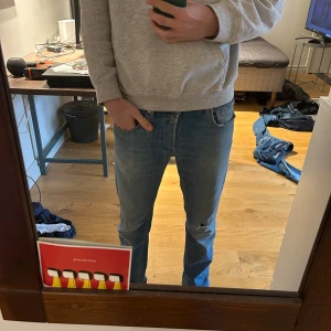 Ljusblå jeansbyxor från replay  - Säljer ett par ljusblå jeans från replay med klassisk femficksdesign och dragkedja. Jeansen har en liten sliten detalj på vänster knä och är i en straight passform. Perfekta för en avslappnad stil.