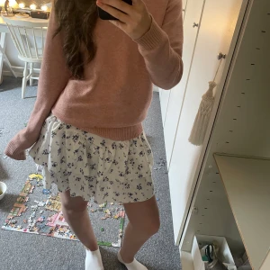 Vit blommig volangkjol - Supersöt vit kjol med blått blommönster och volangdetaljer. Kjolen har en luftig och flowy känsla, perfekt för varmare dagar. Den har en kort längd