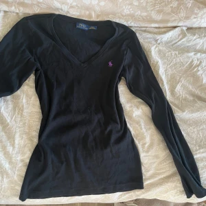 Svart långärmad tröja från Ralph Lauren - Svart långärmad tröja från Ralph Lauren med v-ringning och lila broderad logga på bröstet. 