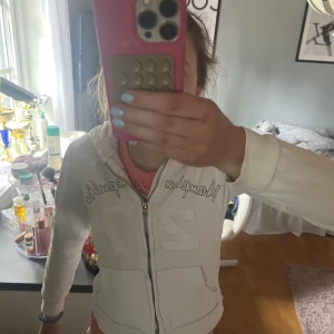 Vit hoodie från Hampton Republic - Säljer en vit hoodie från Hampton Republic med dragkedja och tryck på framsidan. Tröjan har en mysig huva och är tillverkad i en bomulls- och polyesterblandning. Perfekt för en avslappnad stil.