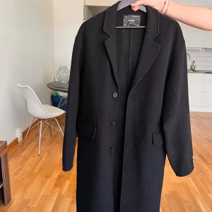 Svart kappa från Axel Arigato - Säljer en stilren svart kappa från Axel Arigato. Klassisk design med krage, knäppning framtill och två fickor. Perfekt för dig som gillar minimalistisk och tidlös stil. Aldrig använd då den är för stor för mig och det är storlek L på den! Passar både kvinnor och män!🤩