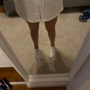 Vita linneshorts från Gina Tricot - Säljer ett par vita shorts från Gina Tricot i luftig linnemix. De har resår i midjan och snörning framtill för en bekväm passform. Perfekta för varma dagar och enkel att matcha med olika toppar.