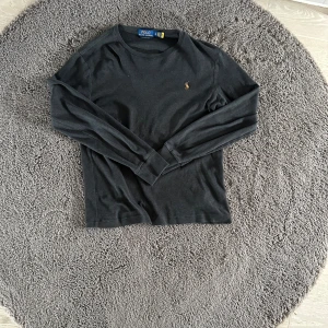 Svart långärmad tröja från Polo Ralph Lauren - Klassisk svart långärmad tröja från Polo Ralph Lauren med liten broderad logga på bröstet. Tröjan har rund halsringning och är tillverkad i mjuk bomull. Perfekt för en stilren och enkel look. Stoleken är S men passar 165-180